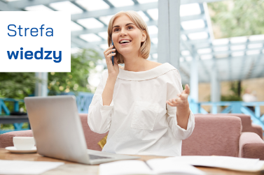 Uśmiechnięta kobieta siedzi przy laptopie, rozmawia przez telefon i gestykuluje. Pracuje przy stoliku w jasnym, przeszklonym wnętrzu. W lewym górnym rogu niebieski napis: „Strefa wiedzy”. Grafika promuje dostęp do materiałów informacyjnych.